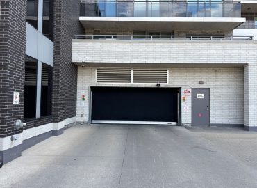 Urban loading-dock area with a large black roll-up garage door, light-gray brick walls, and a small gray door to the right.