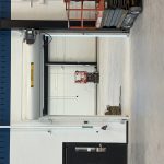 Industrial warehouse interior with a white rolling fire door open, a blue upper wall, and a red scissor lift in the doorway.